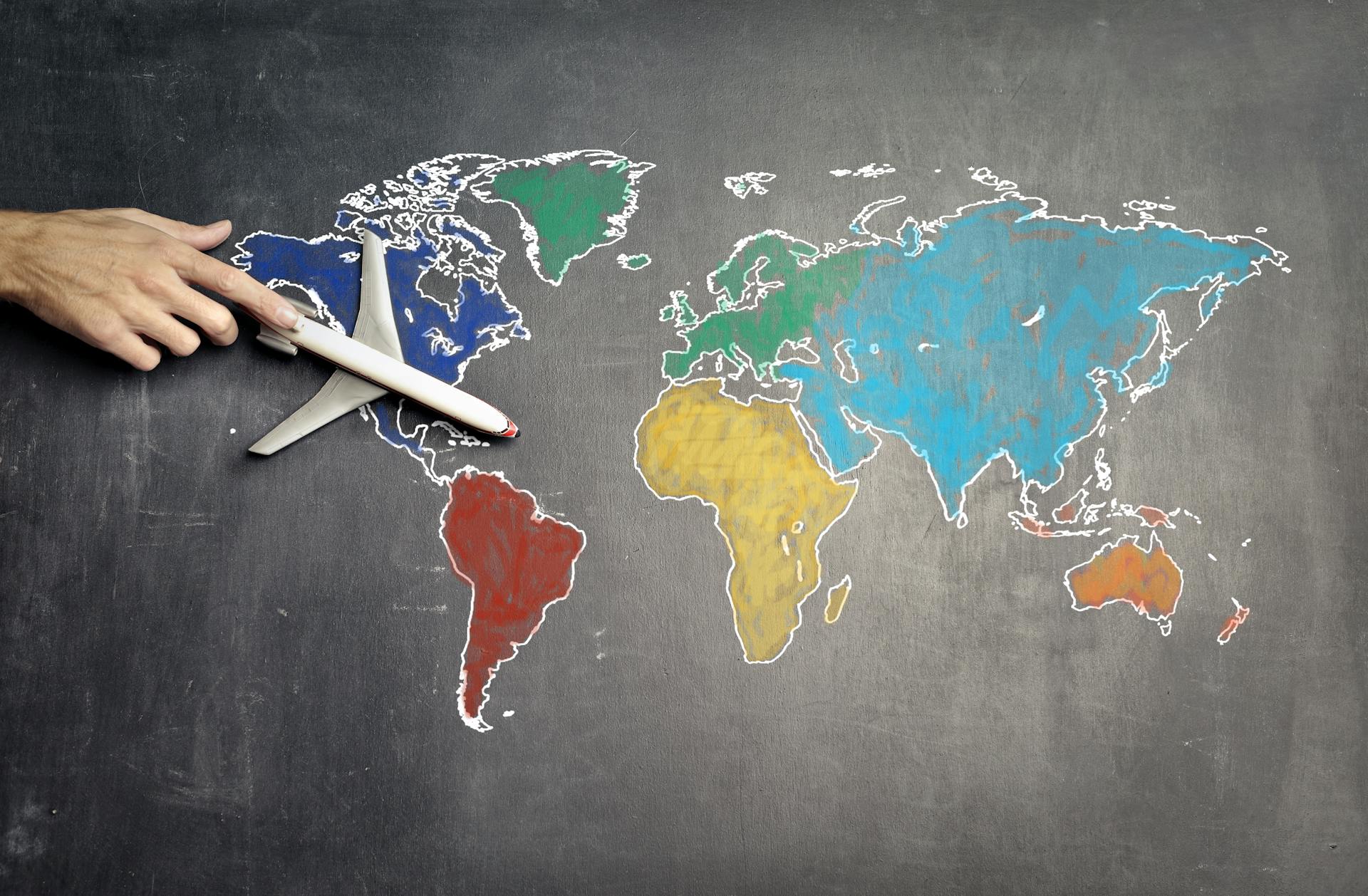 A hand guiding a toy airplane over a colorful world map.